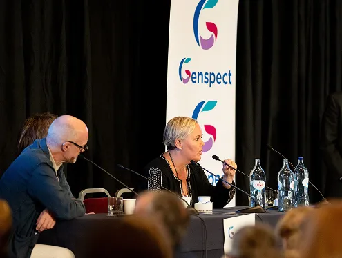 Panel members answer questions using microphone, with Genspect banner in background